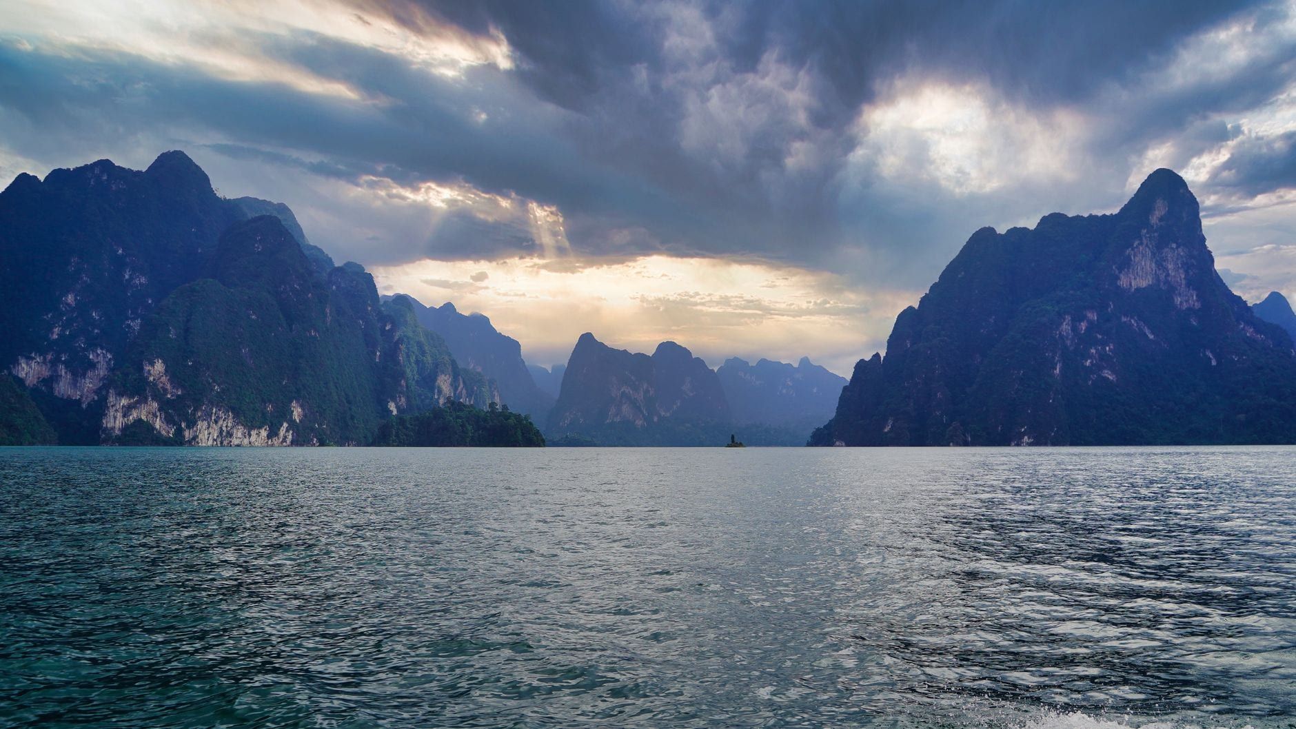 Nubes dramáticas y rayos de sol sobre las montañas de piedra caliza y las aguas tranquilas de Khao Sok.