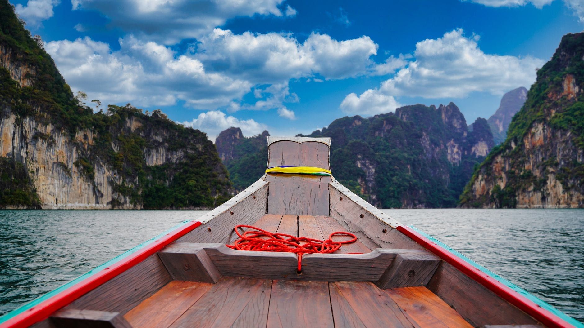 Bote de madera de cola larga navegando por el lago junto a imponentes acantilados de piedra caliza en el Parque Nacional Khao Sok.