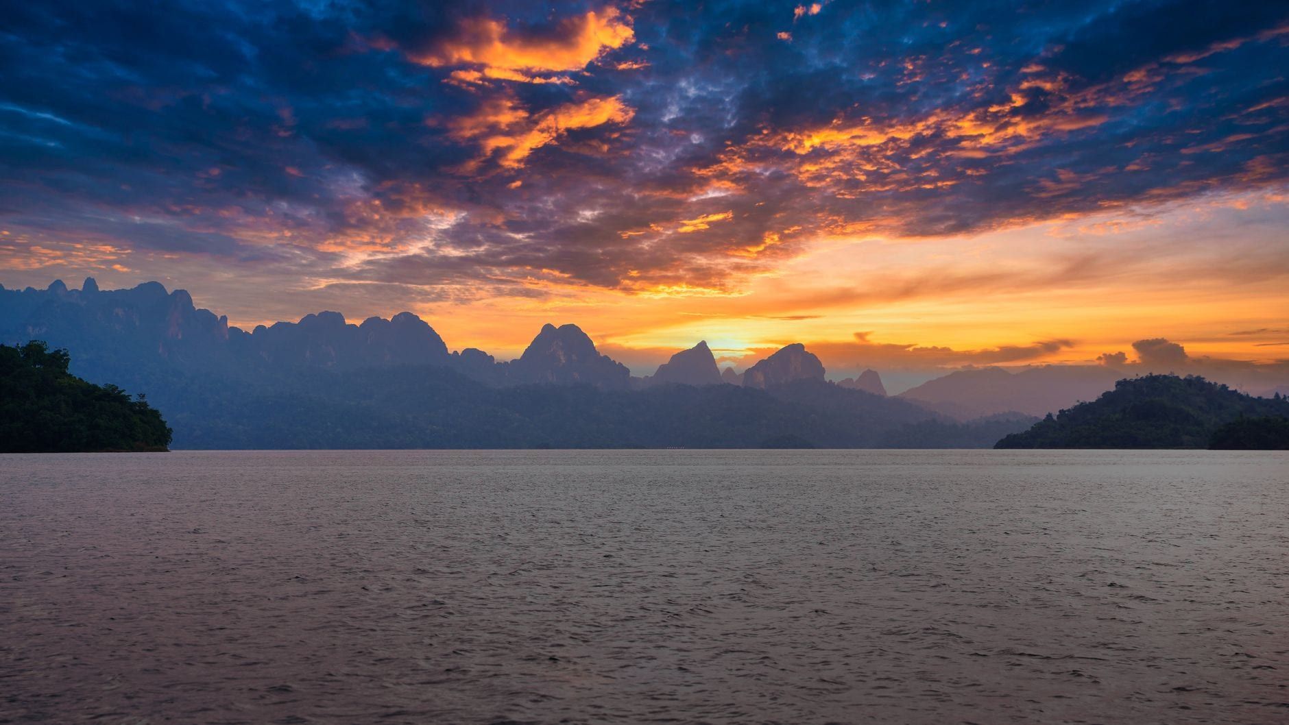 Vibrantes nubes de atardecer de color naranja y púrpura iluminan el cielo sobre el lago tranquilo y las crestas de las montañas en Khao Sok.